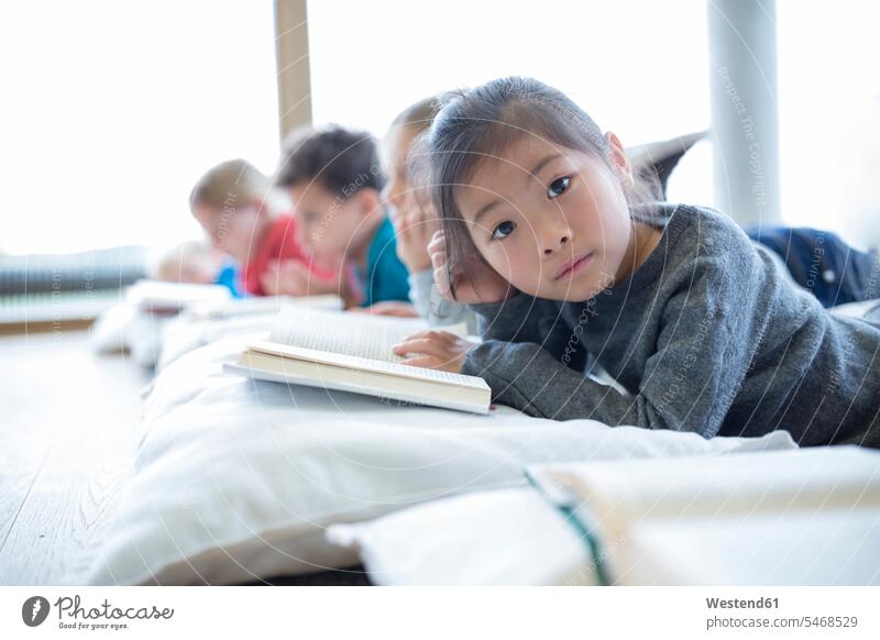 Portrait of schoolgirl lying on the floor with classmates reading book in school break room student pupils floors schools female pupils School Girl schoolgirls