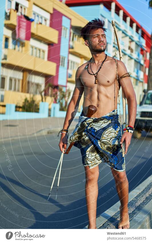 Tribal man with his traditional arch and arrows in the middle of the city with cars passing by, Lubango, Angola African Africans motor vehicles road vehicle