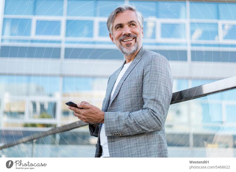 Smiling mature businessman with cell phone outdoors business life business world business person businesspeople Business man Business men Businessmen