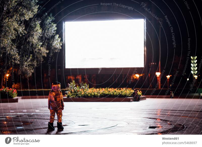 Spaceman on a square at night attracted by shining projection screen astronaut astronauts Projection Screen plaza places Public Square city town cities towns