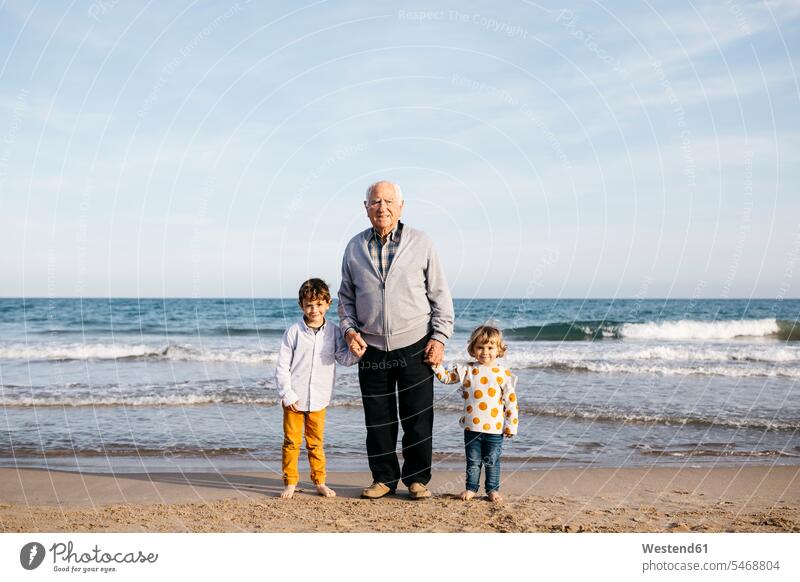 Portrait of happy grandfather standing hand in hand on the beach with his grandchildren Spain senior men senior man elder man elder men senior citizen boy boys