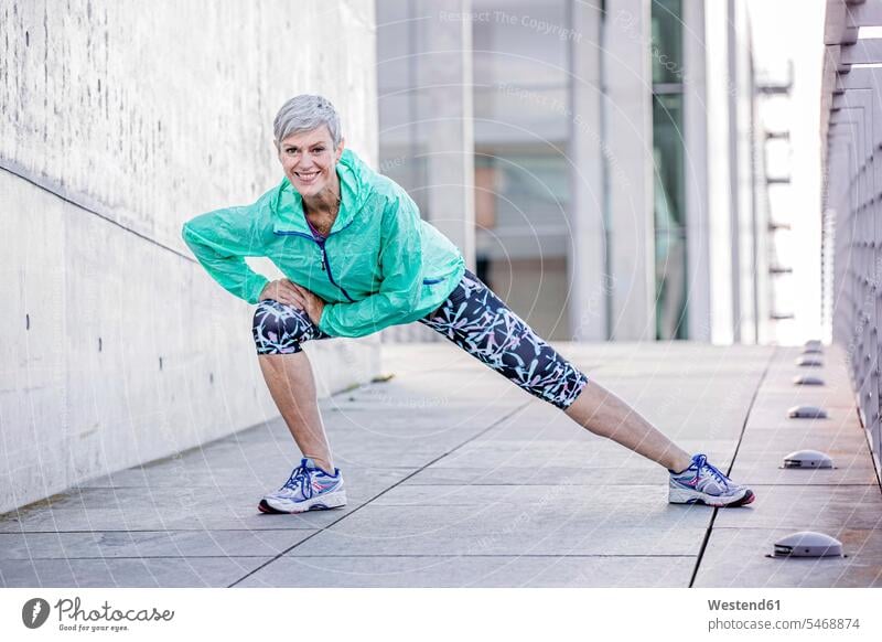 Portrait of smiling mature woman stretching in the city town cities towns portrait portraits females women smile outdoors outdoor shots location shot