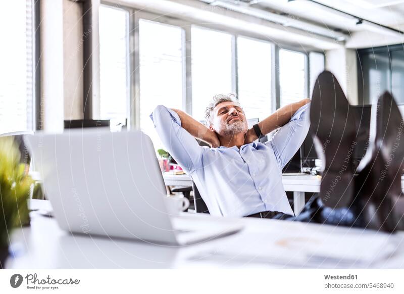 Relaxed mature businessman sitting at desk in office leaning back offices office room office rooms Businessman Business man Businessmen Business men desks