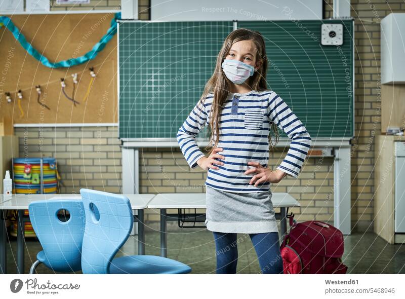 Portrait of confident girl wearing mask in classroom pupils schoolchild schoolchildren blackboards stand healthy protect protecting safe Safety secure buildings