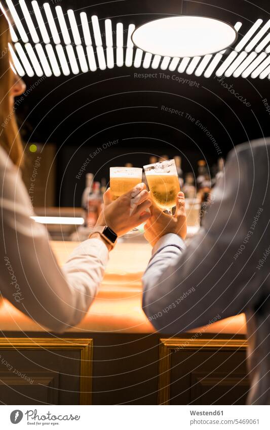 Close-up of couple clinking beer glasses in a bar Beer Glass Beer Glasses toasting cheers Beers Ale bars twosomes partnership couples Drinking Glasses Alcohol