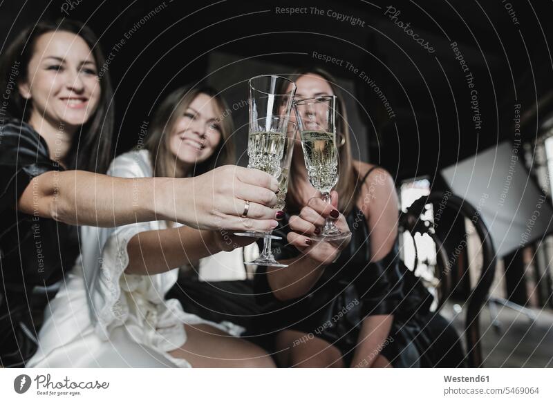 Three happy women sitting on bed clinking champagne glasses female friends toasting cheers Sparkling Wine happiness woman females Seated Champagne Glass