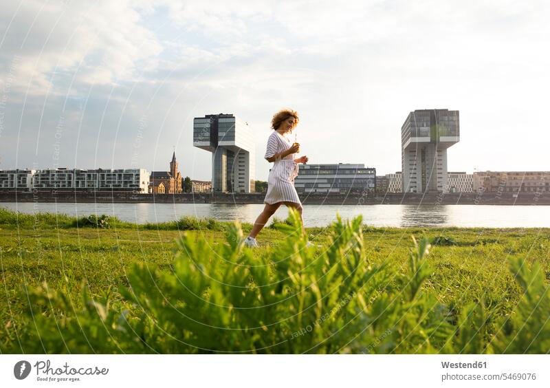 Woman with beer bottle walking on grassy land against river in city at sunset color image colour image Germany leisure activity leisure activities free time