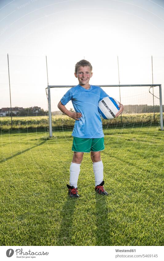 Portrait of smiling young football player holding ball on football ground footballers football players soccer players soccer pitch football pitch portrait