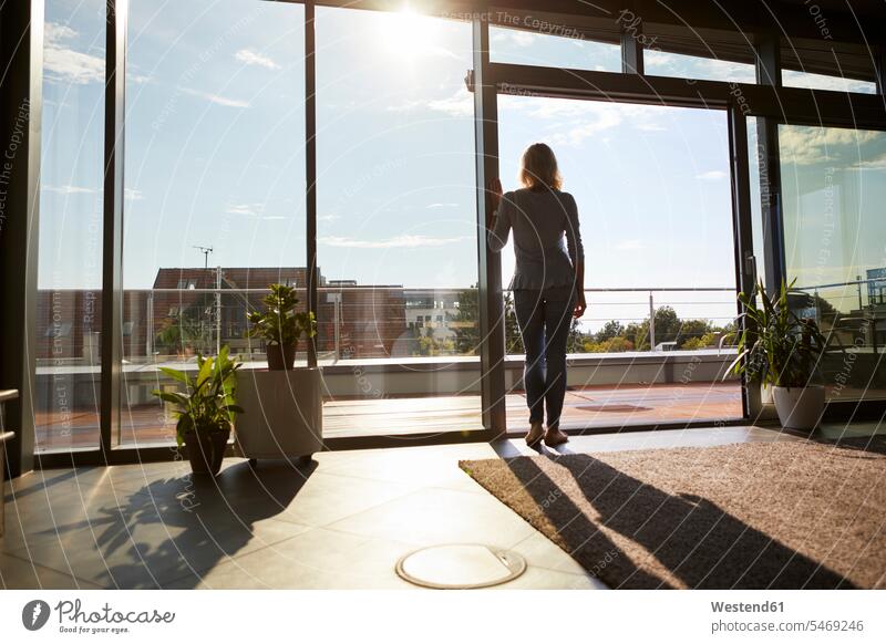 Back view woman in backlight standing at the window at home looking out windows View Vista Look-Out outlook females women Backlit back light back lighting