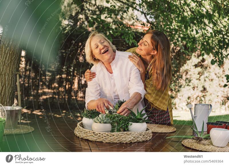 Daughter looking at cheerful mother taking care of plants on table in yard color image colour image Spain leisure activity leisure activities free time