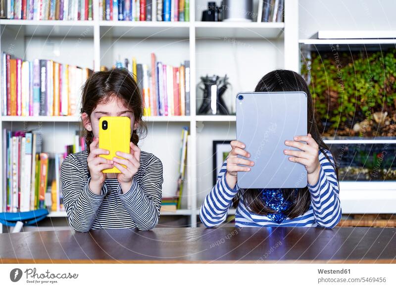 Two sisters sitting side by side at table in the living room using electronic devices Aquaria Aquariums fish tank rack racks Shelve shelves book shelf