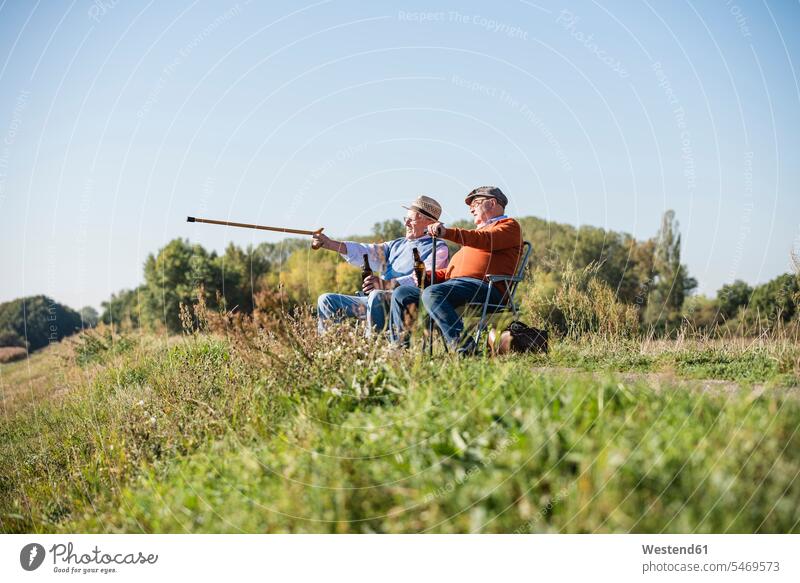 Two old friends sitting in the fields, drinking beer, pointing with walking stick Beer Beers Ale talking speaking Best Friend Best Friends Best Pal Seated Field