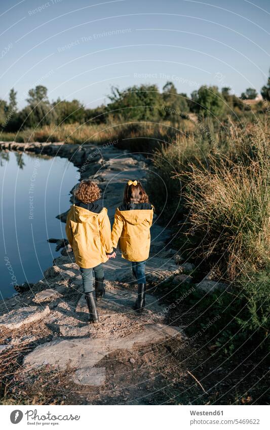 Siblings holding hands while walking on rocks at riverbank color image colour image outdoors location shots outdoor shot outdoor shots Spain 6-7 years