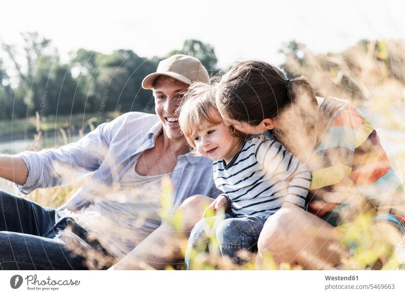 Happy family having fun at the riverside on abeautiful summer day sitting Seated riverbank families happiness happy summer time summery summertime water's edge