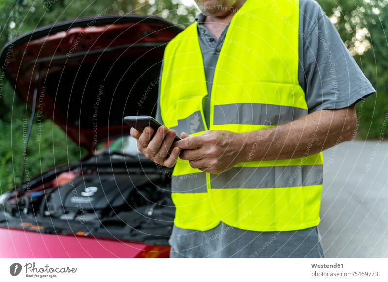 Close up of a senior man standing at his broken car wearing a safety vest and using his smartphone transport motor vehicles road vehicle road vehicles Auto