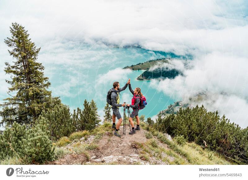 Happy young couple on a hiking trip in the mountains high fiving, Herzogstand, Bavaria, Germany human human being human beings humans person persons