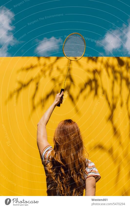 Woman holding badminton racket over yellow wall during sunny day color image colour image outdoors location shots outdoor shot outdoor shots daylight shot