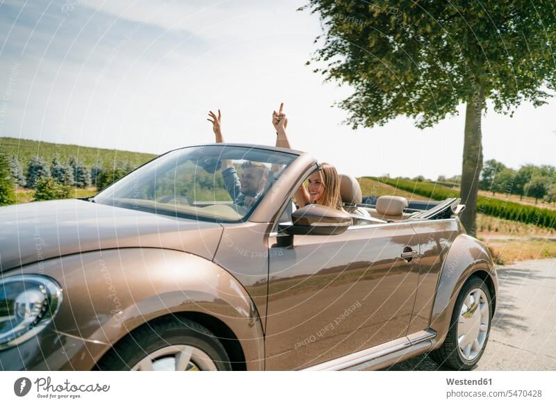 Happy couple driving in convertible car on a country road automobile Auto cars motorcars Automobiles rural road rural roads country roads happiness happy