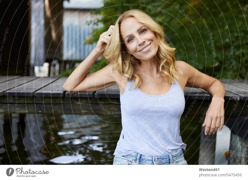 Smiling relaxed woman at wooden jetty at a lake lakes jetties smiling smile females women relaxation water waters body of water Adults grown-ups grownups adult