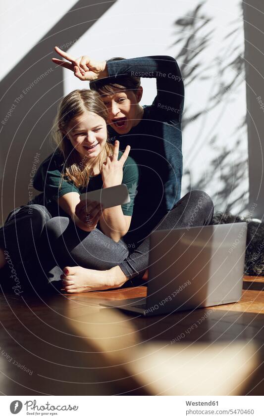 Happy mother and daughter sitting on the floor at home taking a selfie animals creature creatures domestic animal pet Canine dogs computers Laptop Computer