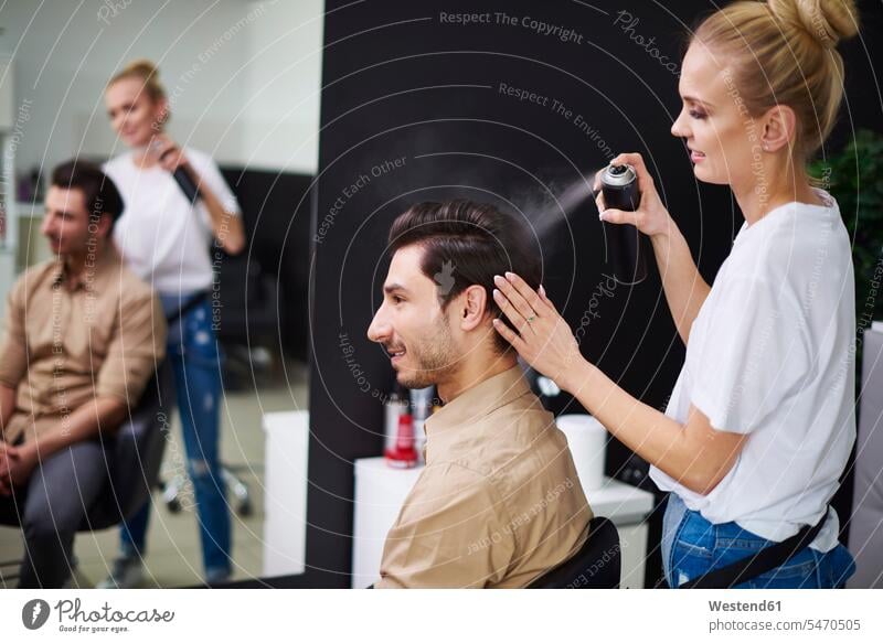 Smiling hairdresser using hairspray on man's hair hair salon hair salons smiling smile female hairdresser hair spray men males people persons human being humans