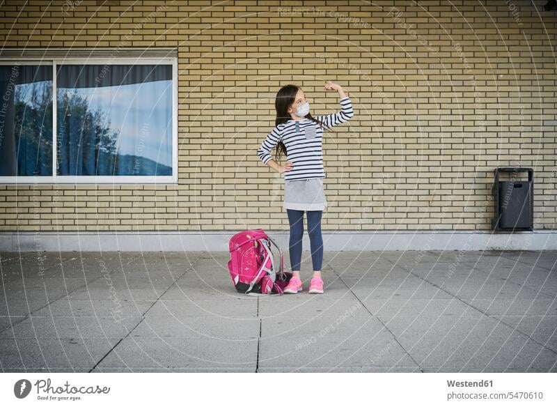 Girl with schoolbag wearing mask standing in front of building flexing her muscles pupils schoolchild schoolchildren windows healthy Force Power Strengthy