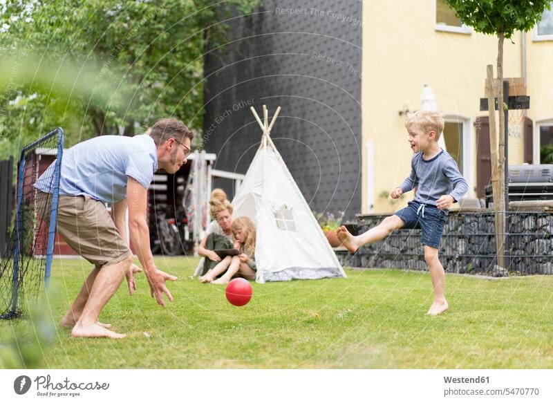 Man and son playing soccer while woman sitting with daughter in tent at back yard during weekend color image colour image Germany outdoors location shots