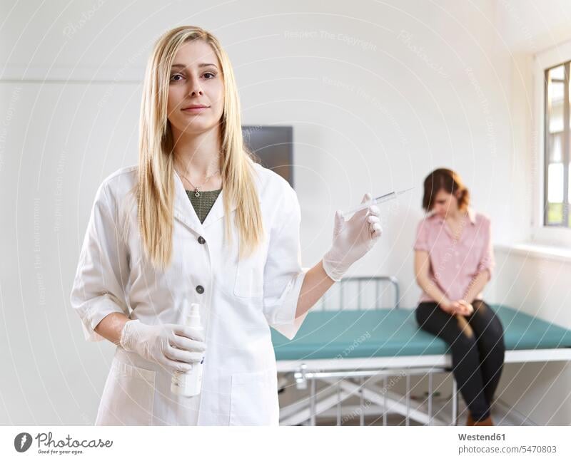 Female doctor with syringe in medical practice and patient in background medical practices Doctors Office Doctor's Office Female Doctor physicians