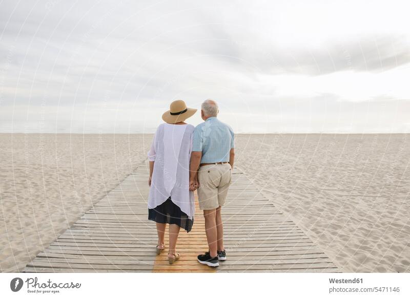 Back view of senior couple standing hand in hand on wooden boardwalk looking at horizon, Liepaja, Latvia associate associates partner partners partnerships