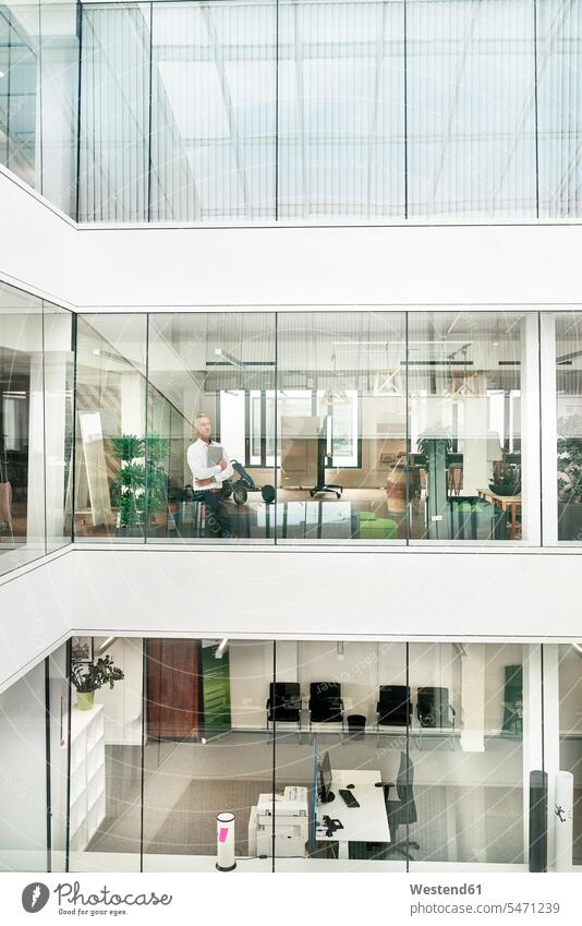 Mature businessman looking out of office building, holding laptop human human being human beings humans person persons caucasian appearance caucasian ethnicity