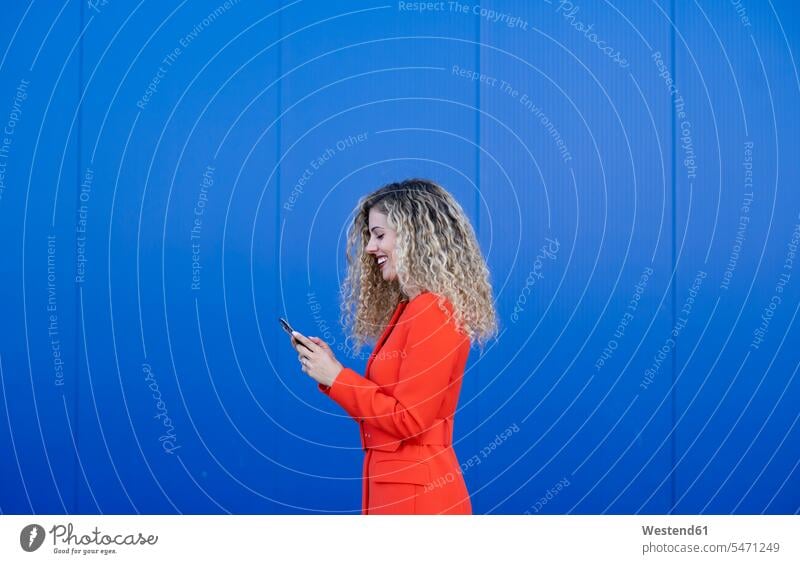 Profile of young woman wearing red dress in front of blue background looking at cell phone human human being human beings humans person persons