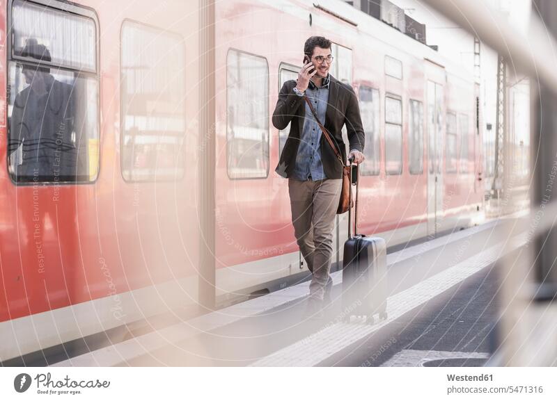 Smiling young man on cell phone walking on station platform along commuter train going smiling smile men males mobile phone mobiles mobile phones Cellphone