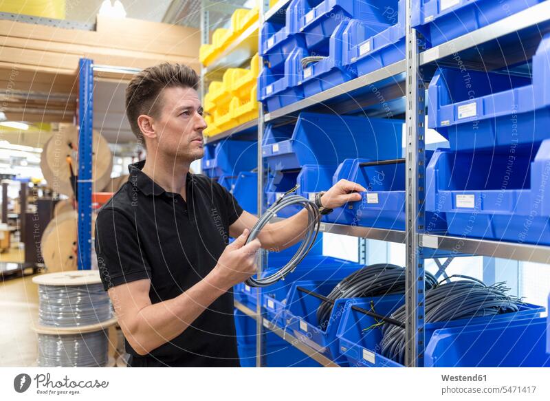 Man holding cable in factory storeroom power cord cables man men males storage room stockroom factories Adults grown-ups grownups adult people persons