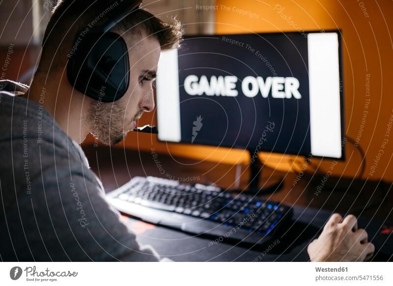 Young man sitting at his PC, looking at screen with game over text headphones headset tension computer game computer games compulsive gambling word words