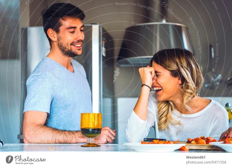 Laughing young woman with boyfriend in kitchen at home Drinking Glass Drinking Glasses cook speak speaking talk delight enjoyment Pleasant pleasure Cheerfulness