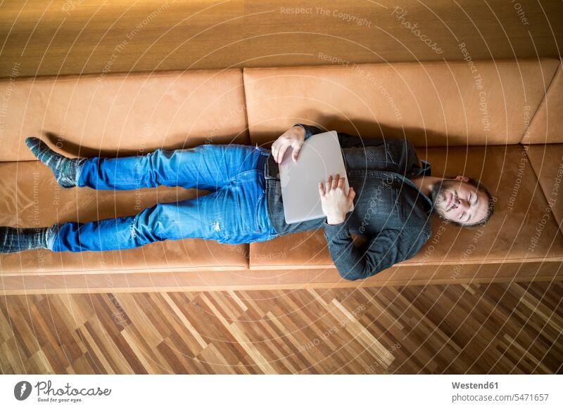 Man with laptop relaxing on couch man men males lying laying down lie lying down relaxation Laptop Computers laptops notebook settee sofa sofas couches settees