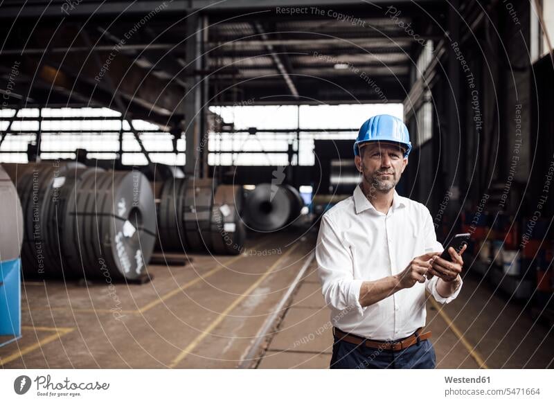 Businessman holding smart phone while standing in factory color image colour image indoors indoor shot indoor shots interior interior view Interiors steel mill