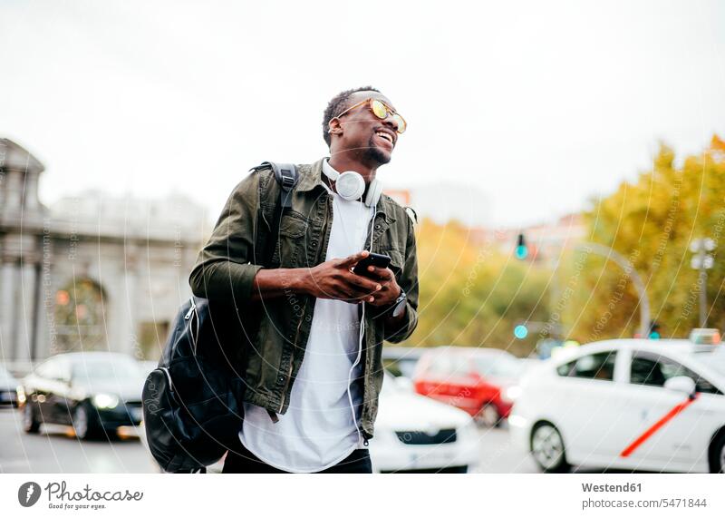 Happy man wearing sunglasses holding smart phone while standing against sky in city color image colour image Spain leisure activity leisure activities free time