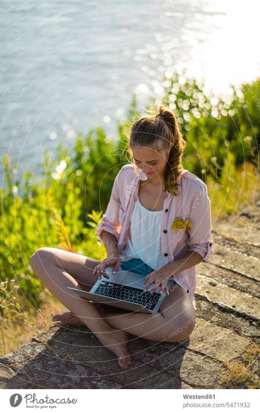 Woman sitting at the riverside in summer using laptop Laptop Computers laptops notebook summer time summery summertime portrait portraits riverbank Seated River