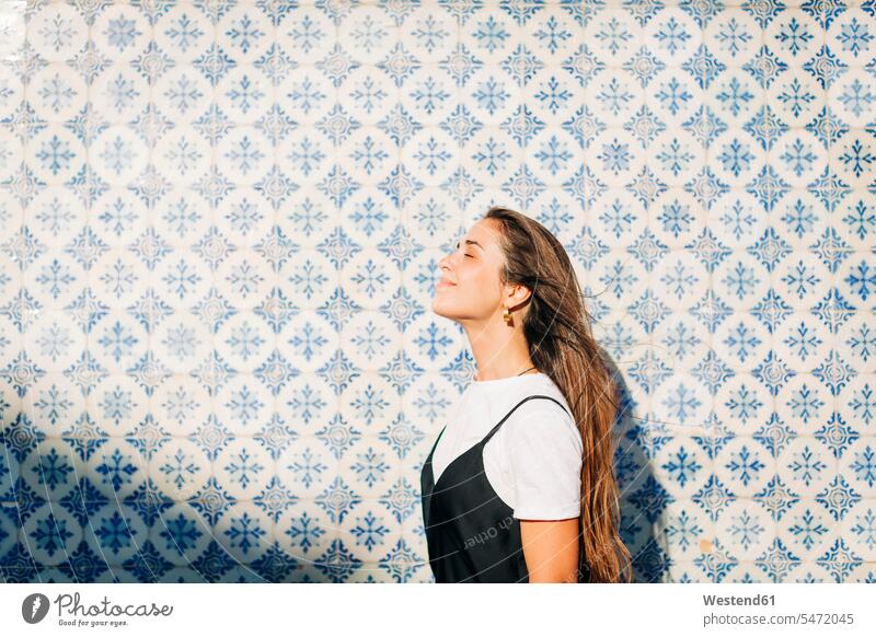 Smiling beautiful woman with eyes closed standing by tiled wall on sunny day color image colour image Portugal leisure activity leisure activities free time