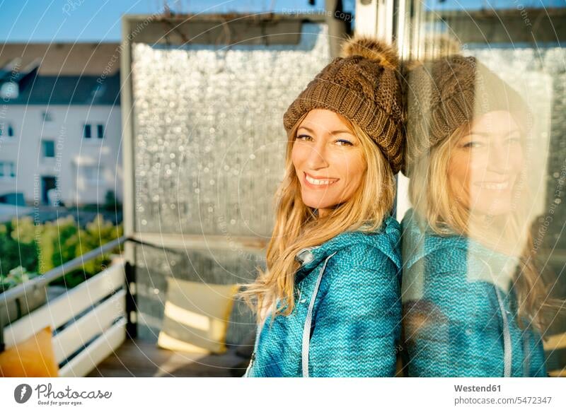 Portrait of smiling blond mature woman wearing bobble hat on balcony portrait portraits bobble cap blond hair blonde hair smile females women balconies people