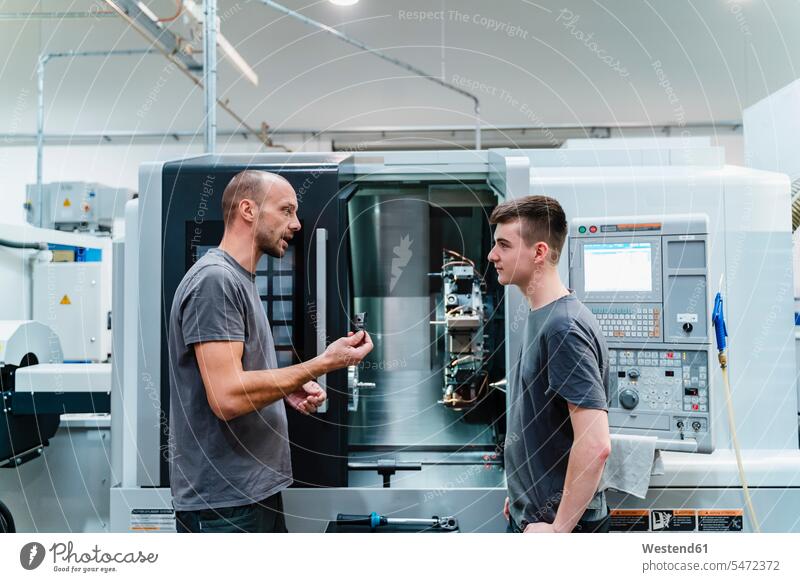 Maintenance engineer giving instruction to coworker while standing against machinery at industry color image colour image indoors indoor shot indoor shots