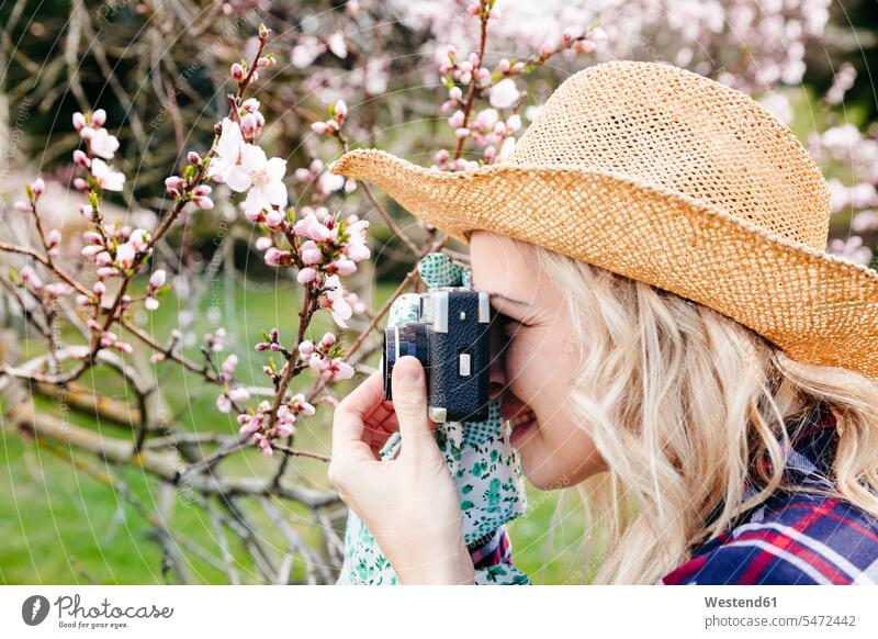 Young woman with a straw hat taking pictures in the garden with an old camera images photo photographs photos hats straw hats domestic garden gardens analog