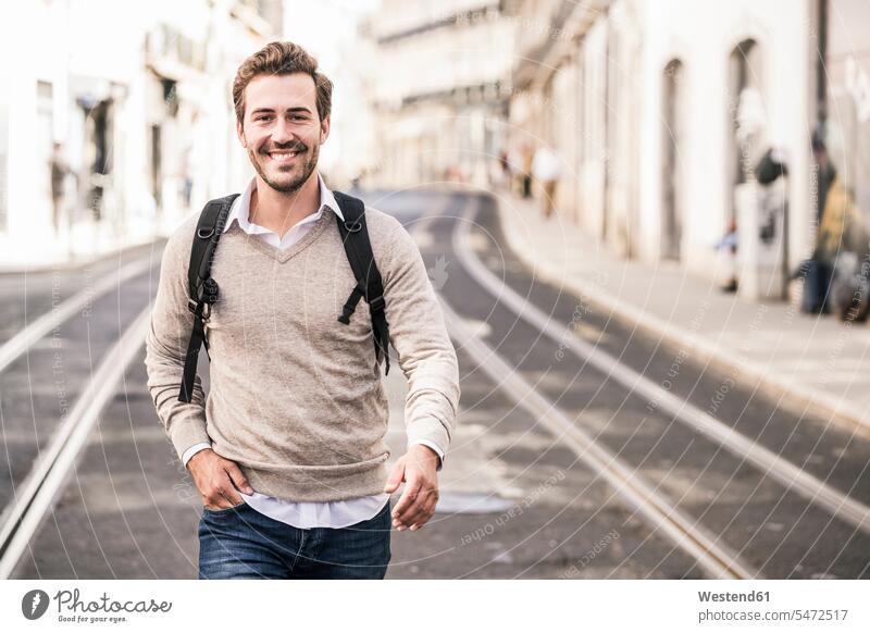 Portrait of smiling young man with backpack in the city on the go, Lisbon, Portugal touristic tourists back-pack back-packs backpacks rucksack rucksacks jumper