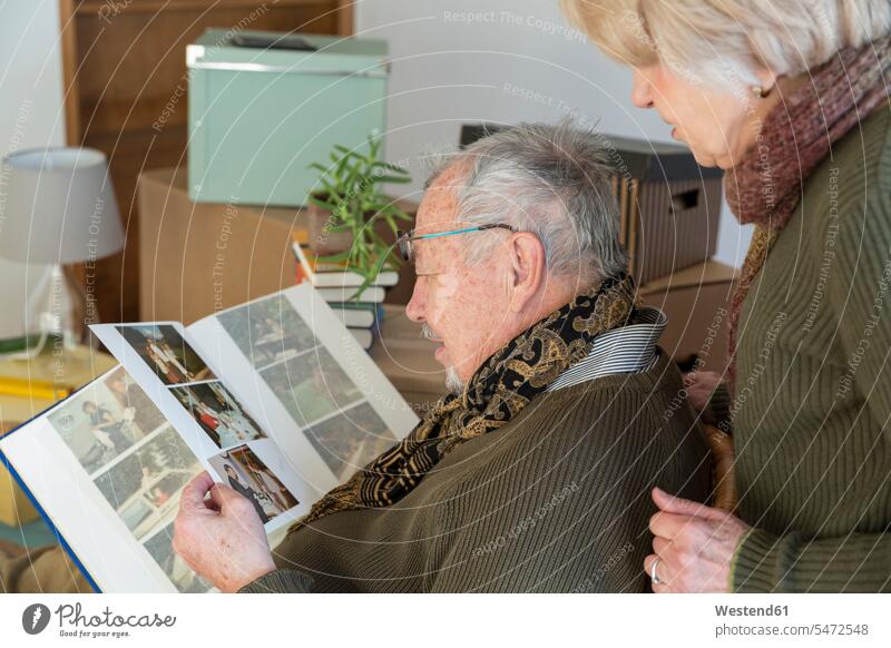 Senior couple looking at photo album surrounded by cardboard boxes in an empty room human human being human beings humans person persons caucasian appearance