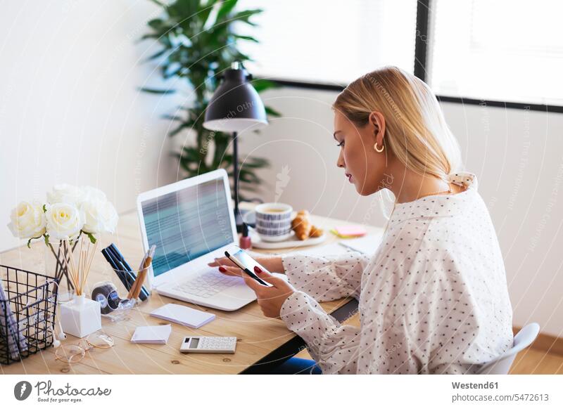 Blond businesswoman sitting at desk, working checking office offices office room office rooms Seated At Work blond blond hair blonde hair businesswomen