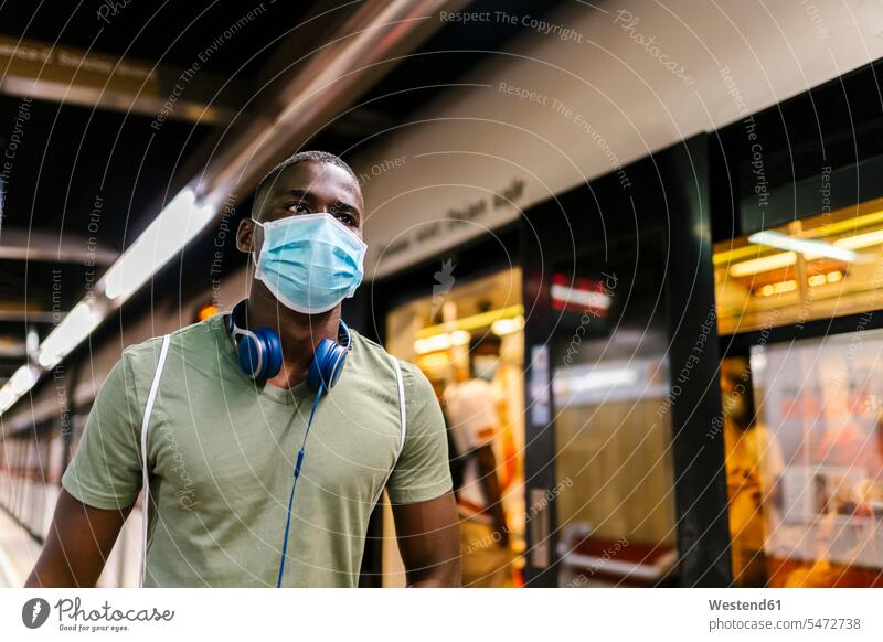 Young man wearing mask looking away while standing at subway station color image colour image Spain casual clothing casual wear leisure wear casual clothes