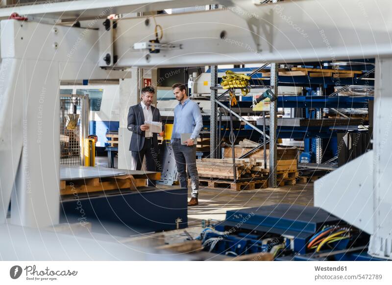 Businessman holding paper while explaining to colleague at factory color image colour image indoors indoor shot indoor shots interior interior view Interiors