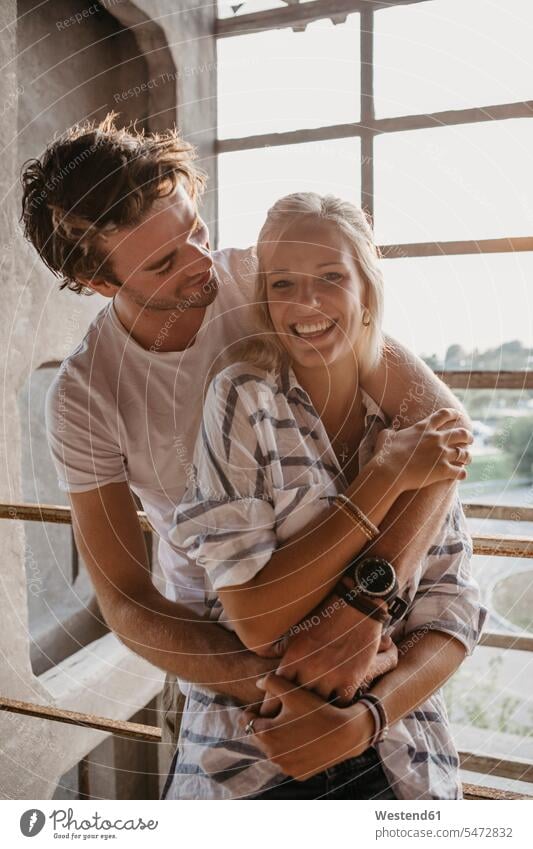 Happy young couple cuddling at the window windows snuggle cuddle snuggling twosomes partnership couples happiness happy people persons human being humans