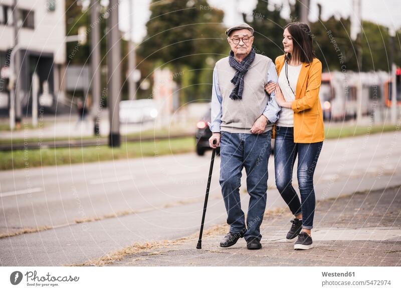 Adult granddaughter assisting her grandfather strolling with walking ...